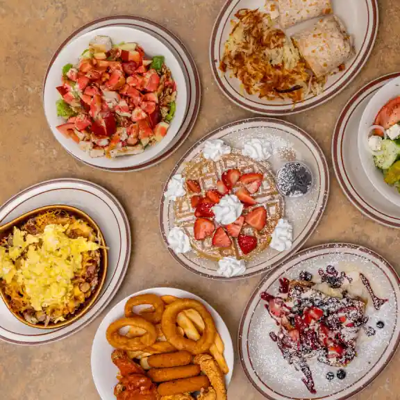 Sampler platter of small dishes including strawberries, shrimp, wings, salad, and pancakes