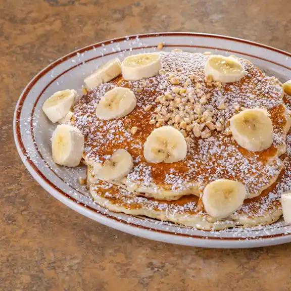 Banana pancake topped with sliced bananas, walnuts, and powdered sugar